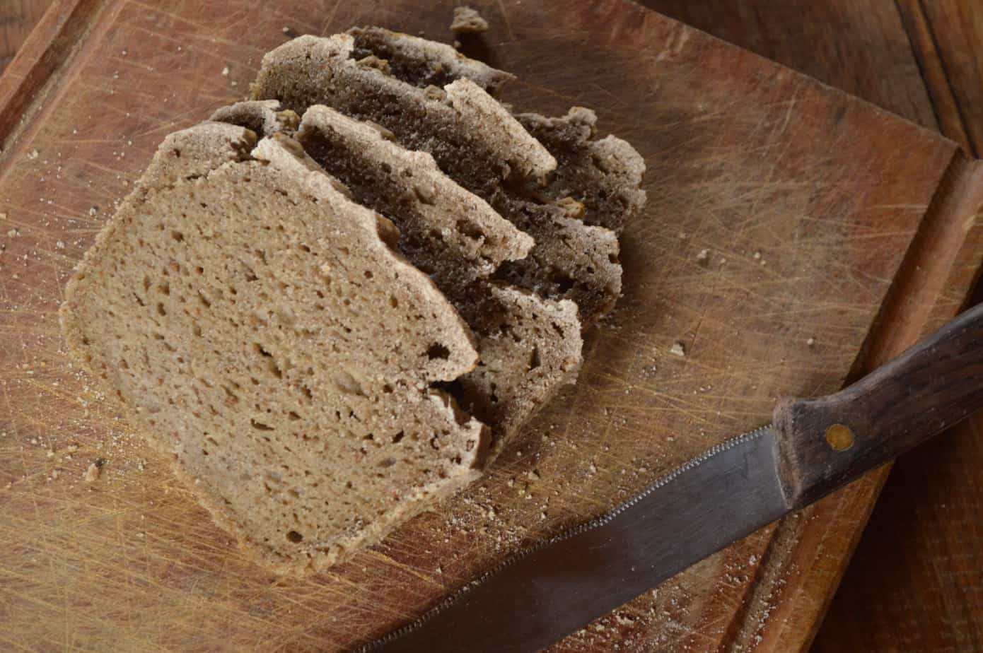 Pan de centeno casero en rebanadas sobre tabla de madera con cuchillo.