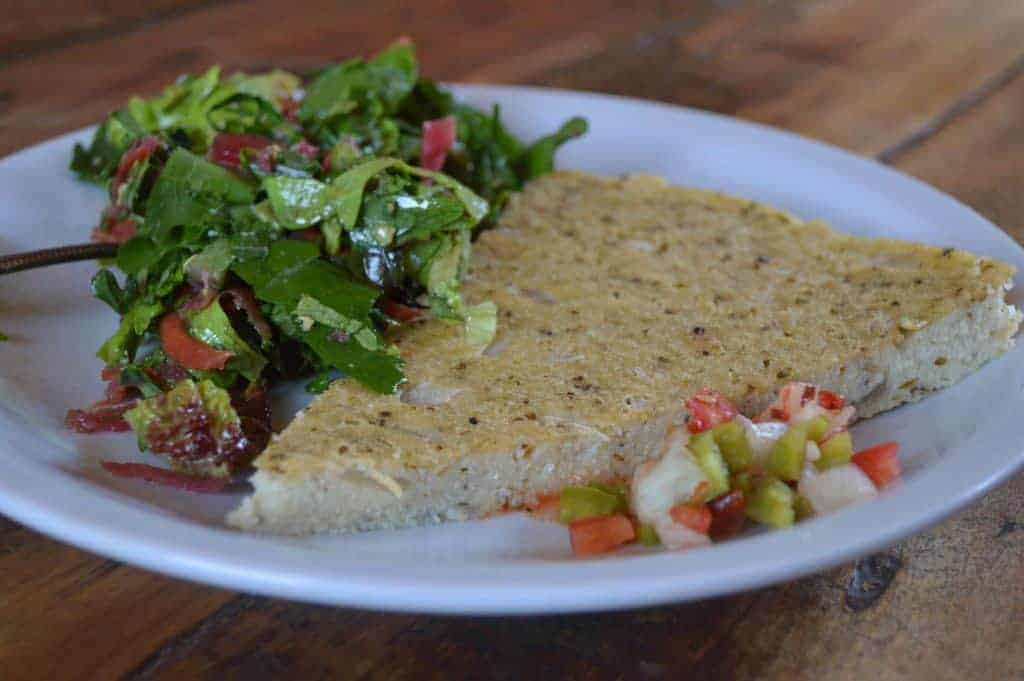 Imagen de una porción de pastel de maíz acompañado de ensalada fresca y salsa de tomate y cebolla.