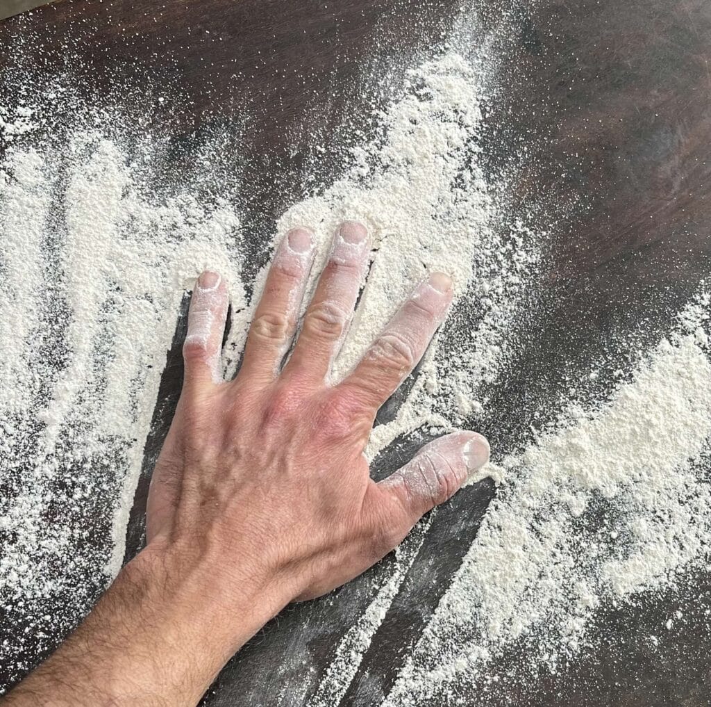 Mano sobre harina de cebada en mesa de cocina.