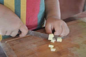 Niño picando queso en la cocina para promover una alimentación saludable.